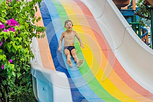 Young boy or kid has fun splashing into pool after going down water slide during summer