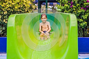 Young boy or kid has fun splashing into pool after going down water slide during summer