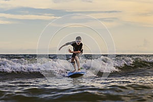 Young boy kid surfer riding waves with a soft board in Rayong beach, Thailand. Rookie surfboard student playing on water in