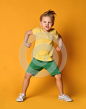 Young boy kid in yellow t-shirt and green shorts poses act like an angry giant monster demonstrates power and hisses with rage