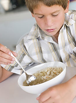 Young boy in kitchen eating soup