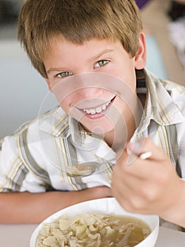 Young boy in kitchen eating soup and smiling