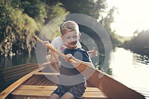 Young boy learning to paddle canoe with his dad