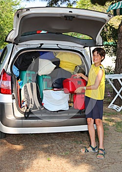 Young boy loads the luggage in the trunk of his car