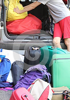 young boy loads the trunk of the car with a lot of luggage