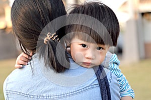 Young boy looking over mother`s shoulder