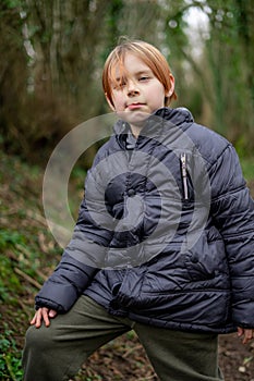 A young boy looks seriously into the camera. A boy of nine years old with long red hair in a warm outdoors jacket. vertical photo