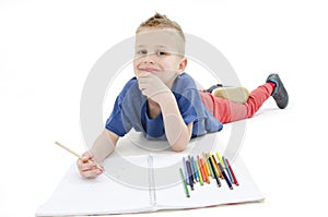 Young boy lying on floor with pencils on a sketch book with a look of concentration, close up view.