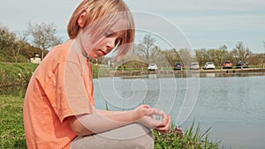 A young boy is meditating outdoors. A boy with red hair sits in a lotus position near a lake. Relaxation, rejuvenation. Side view