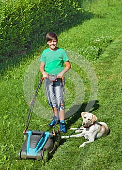 Young boy mowing the lawn accompanied by his labrador doggie