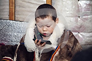 A young boy in the national winter clothes of the northern inhabitants of the tundra, takes a selfie on a smartphone