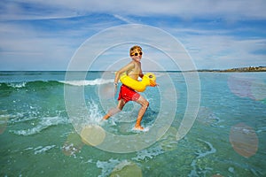 Happy boy run with inflatable duck in ocean at the beach