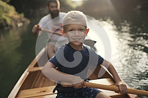 Young boy paddling canoe on the lake with his dad