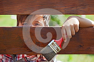 Young boy painting the wooden fence