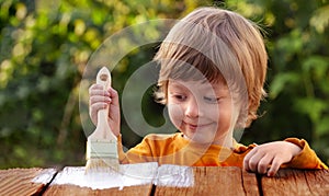 Young boy painting the wooden fence in summer garden