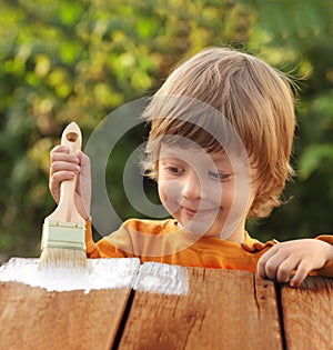 Young boy painting the wooden fence in summer garden