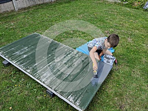 Young boy paints a garden fence panel grey