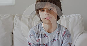 Young boy in pajamas sitting on white couch during morning hours