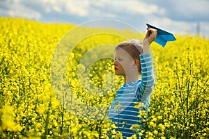 Young Boy with paper Plane against blue sky and Yellow Field Flo