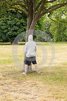 Young boy pisses on a tree in a park