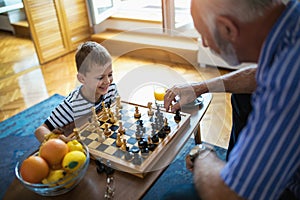 Young boy is playing chess with his grandfather