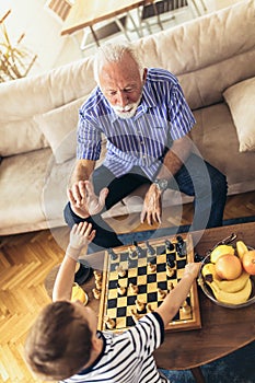 Young boy is playing chess with his grandfather