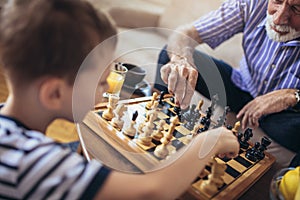 Young boy is playing chess with his grandfather