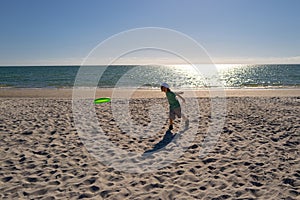 Young boy playing frisbee on beach. Child plays frisbee on the sand on beach near sea. Beach games and active toddler