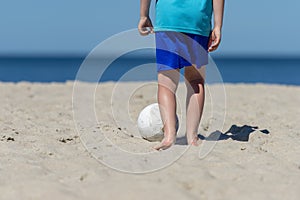 Young boy playing soccer on beach. Summer sport concept