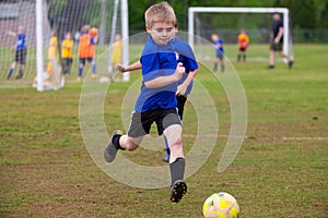 Young boy in blue uniform running to soccer ball on field during game