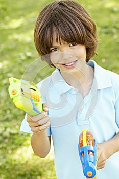 Young Boy Playing With Water Pistols In Park