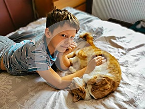 Young boy plays with a funny ginger cat