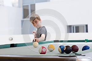 Young boy plays pool billiard, aiming the ball, at terrace, outdoor.
