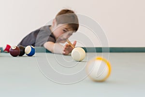 Young boy plays pool billiard, aiming the ball, at terrace, outdoor.