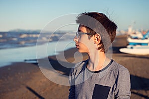 Young boy posing at the summer beach. Cute calm spectacled 12 years old boy at seaside, lokking at sea. Kid`s outdoor portrait in