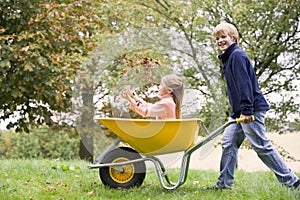 Young boy pushing girl in wheelbarrow