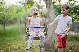 Young boy pushing toddler sister on swing