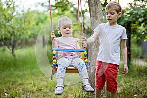 Young boy pushing toddler sister on swing