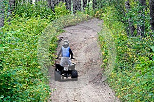 A young boy quads up a hill through the forest