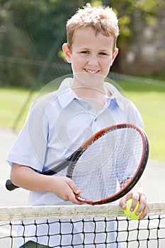 Young boy with racket on tennis court smiling