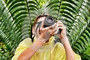 Young boy in raincoat taking photos in forest during field trip