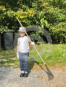 Young boy is raking garbage near his house. Concept of harvesting and autumn renewal.