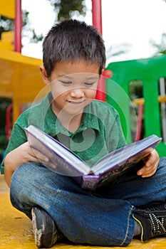 Young boy reading book in a playground