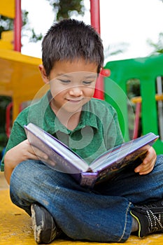 Young boy reading book in a playground photo