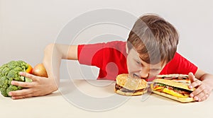 Young boy in red at the table chooses between fastfood and healthy diet on white background