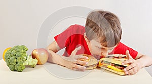 Young boy in red at the table chooses between fastfood and vegetable and fruits