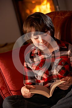 Young Boy Relaxing With Book By Cosy Log Fire