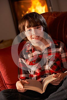 Young Boy Relaxing With Book By Cosy Log Fire