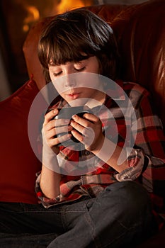 Young Boy Relaxing With Hot Drink By Cosy Log Fire
