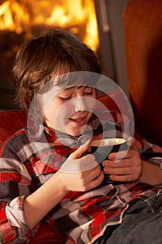 Young Boy Relaxing With Hot Drink By Cosy Log Fire